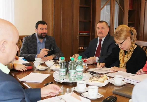 Członkowie Zarządu Powiatu w Płocku uczestniczą w spotkaniu, przy stole z napojami i słodkościami, prowadząc dyskusję i notując uwagi.