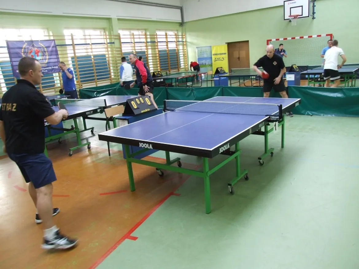 Otwarte zawody w tenisie stołowym, w trakcie których zawodnicy rywalizują przy stołach w sali sportowej.
