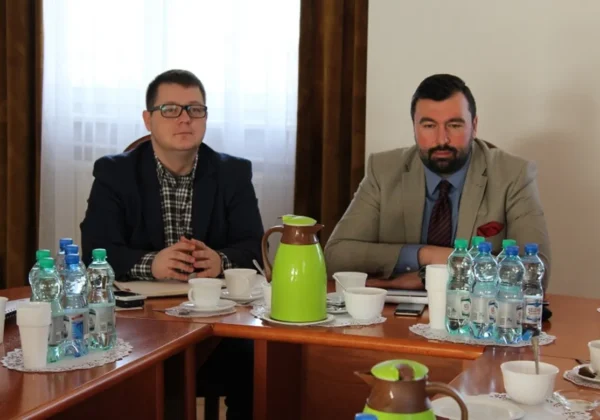 Na zdjęciu dwóch mężczyzn siedzi przy stole w trakcie spotkania dotyczącego przebudowy drogi powiatowej nr 2974W Soczewka – Łąck, z filiżankami i butelkami wody na stole.