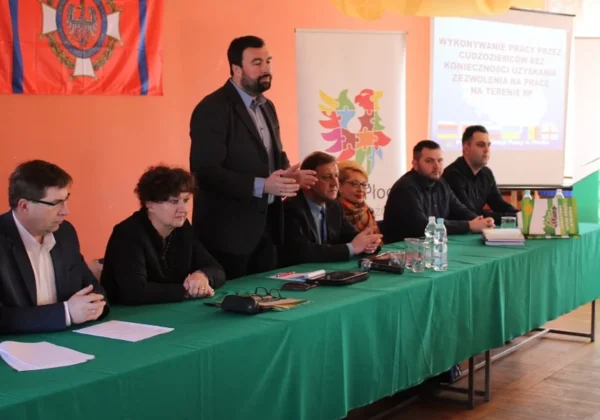 Na zdjęciu przedstawiono panel dyskusyjny, podczas którego omawiane są kwestie zatrudniania cudzoziemców w Polsce, z widocznymi uczestnikami debaty oraz prezentacją na tle flagi.