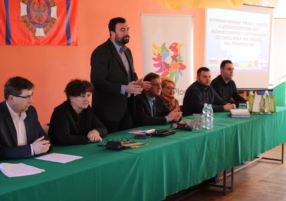 Na zdjęciu przedstawiono panel dyskusyjny, podczas którego omawiane są kwestie zatrudniania cudzoziemców w Polsce, z widocznymi uczestnikami debaty oraz prezentacją na tle flagi.