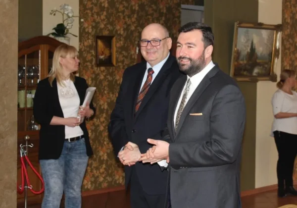 Trzy osoby – dwóch mężczyzn w garniturach i kobieta w czarnym żakiecie – stoją w eleganckim wnętrzu podczas Dnia Kobiet w Powiecie Płockim.