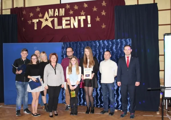 Na zdjęciu widoczna jest grupa uczestników i jurorów występujących w programie "Mam Talent!" w Zespole Szkół im. Jana Śniadeckiego w Wyszogrodzie, stojących przed banerem z nazwą wydarzenia.