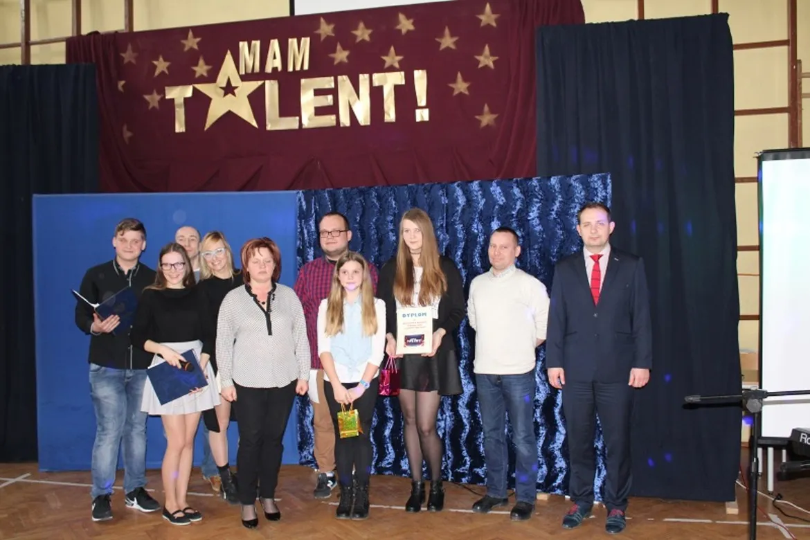 Na zdjęciu widoczna jest grupa uczestników i jurorów występujących w programie "Mam Talent!" w Zespole Szkół im. Jana Śniadeckiego w Wyszogrodzie, stojących przed banerem z nazwą wydarzenia.