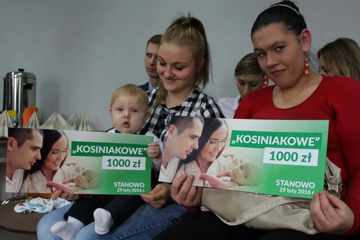 Na zdjęciu widać grupę rodziców z dziećmi trzymających plakaty informujące o programie „kosiniakowe”, które zostały wręczone w powiecie płockim.