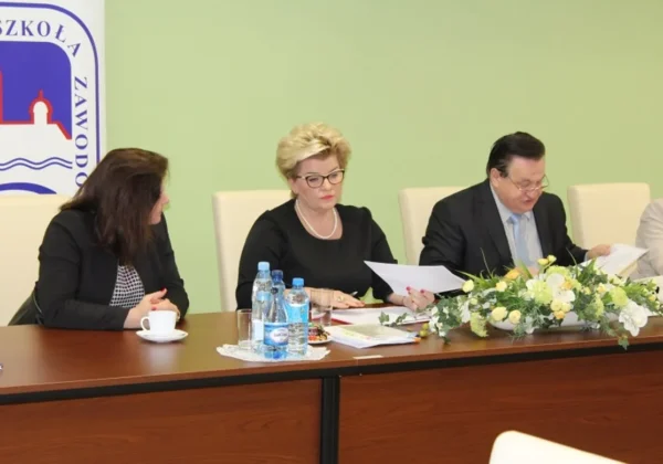 Na zdjęciu przedstawiono uczestników nadzwyczajnego posiedzenia Konwentu Państwowej Wyższej Szkoły Zawodowej w Płocku, siedzących przy stole z dokumentami i kwiatami.