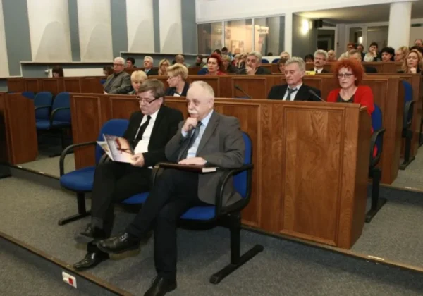 Uczestnicy konferencji „Ratujmy gimnazja” siedzą na wykładzie w sali z drewnianymi elementami, skupieni na prelekcji.