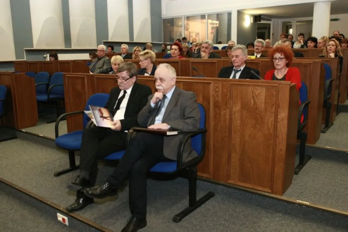 Uczestnicy konferencji „Ratujmy gimnazja” siedzą na wykładzie w sali z drewnianymi elementami, skupieni na prelekcji.