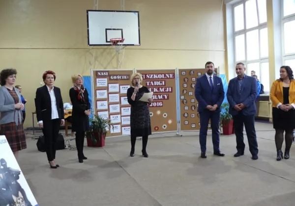 VI Szkolne Targi Edukacji i Pracy w Zespole Szkół im. Stanisława Staszica w Gąbinie, z prezentacją mówców stojących przy tablicy informacyjnej.