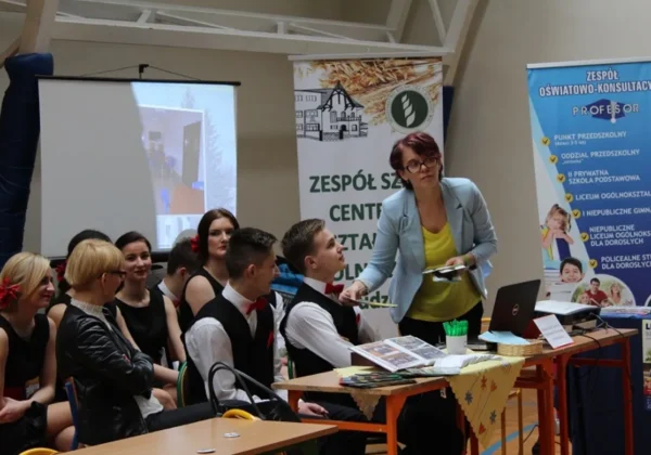 Na zdjęciu prezentowane są uczestnicy III Targów Edukacyjnych w Słupnie 2016, w tym kobieta prowadząca prezentację oraz grupa młodych ludzi w strojach eleganckich.