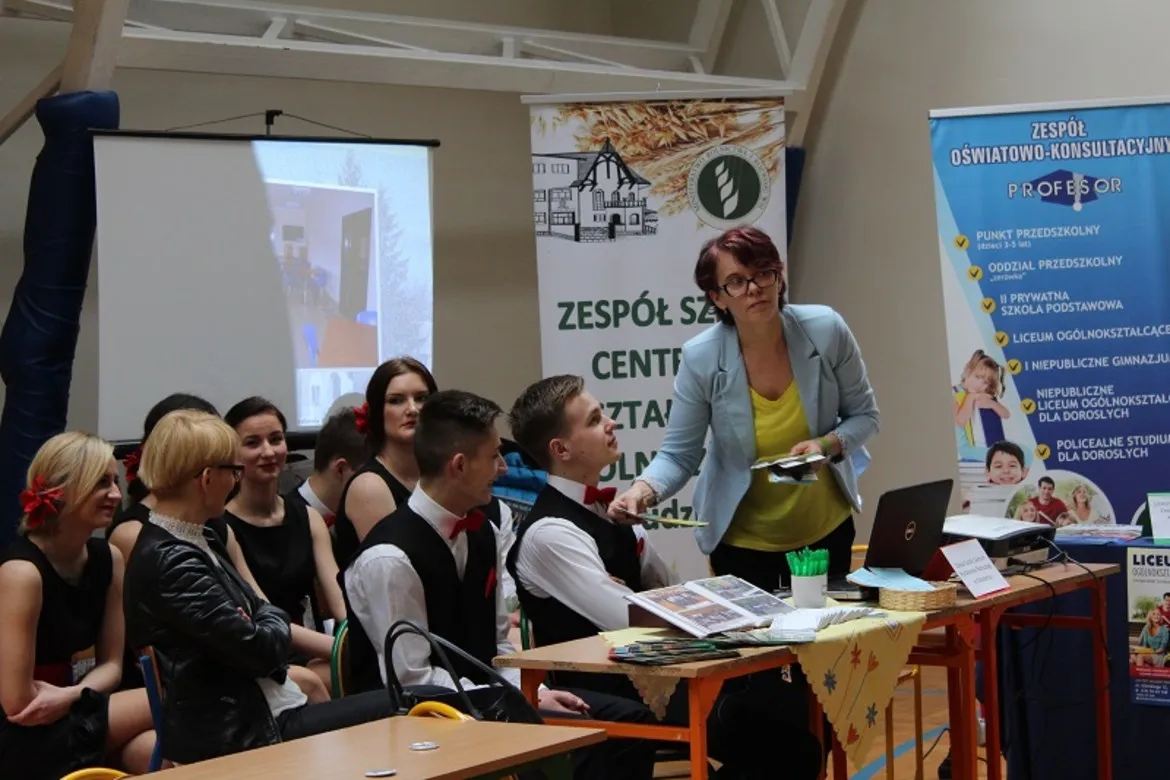 Na zdjęciu prezentowane są uczestnicy III Targów Edukacyjnych w Słupnie 2016, w tym kobieta prowadząca prezentację oraz grupa młodych ludzi w strojach eleganckich.
