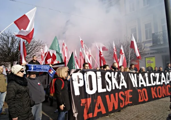 Na zdjęciu widoczny jest tłum ludzi podczas manifestacji upamiętniającej Żołnierzy Wyklętych, trzymających flagi Polski oraz banner z hasłem "POLSKA WALCZĄCA ZAWSZE DO KOŃCA".