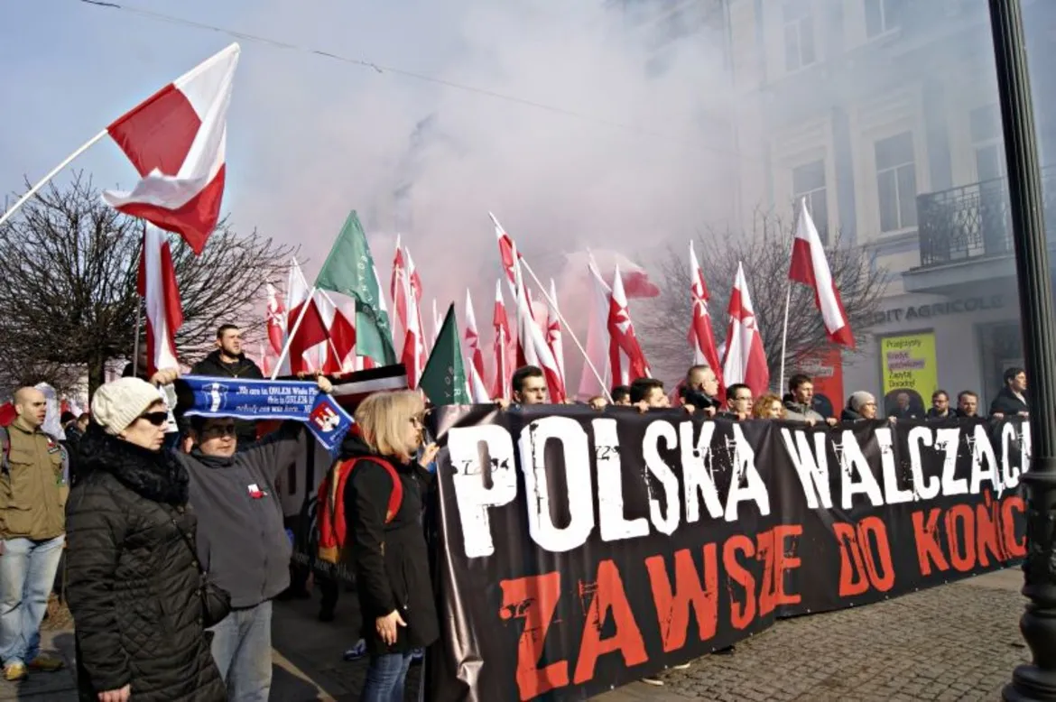 Na zdjęciu widoczny jest tłum ludzi podczas manifestacji upamiętniającej Żołnierzy Wyklętych, trzymających flagi Polski oraz banner z hasłem "POLSKA WALCZĄCA ZAWSZE DO KOŃCA".