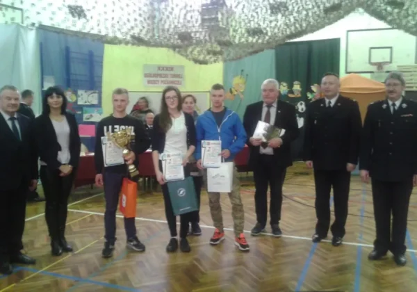 Zdjęcie przedstawia laureatów Ogólnopolskiego Konkursu Wiedzy Pożarniczej w powiecie płockim, którzy stoją z nagrodami i dyplomami w towarzystwie organizatorów wydarzenia.