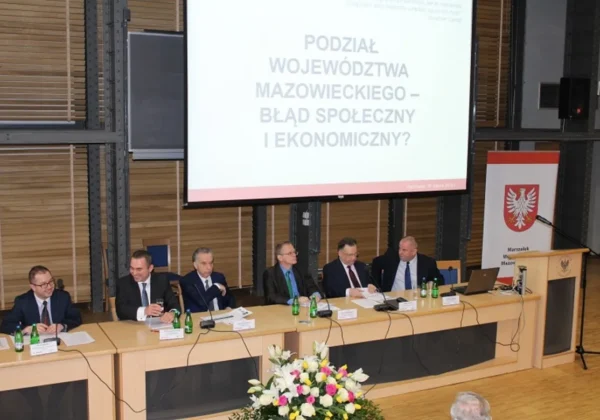 Na zdjęciu przedstawiono panel dyskusyjny dotyczący podziału Województwa Mazowieckiego, z prominentnymi uczestnikami oraz prezentacją na temat społecznych i ekonomicznych skutków tego podziału.