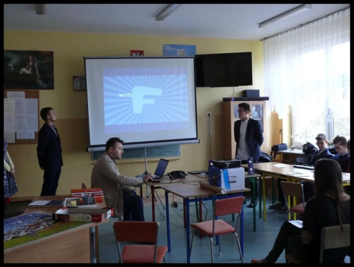 Uczniowie i nauczyciele uczestniczą w prezentacji dotyczącej bezpieczeństwa w internecie w klasie.