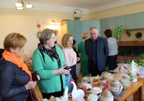 Uczestnicy spotkania wielkanocnego w DPS podziwiają dekoracje i rękodzieło na stole.