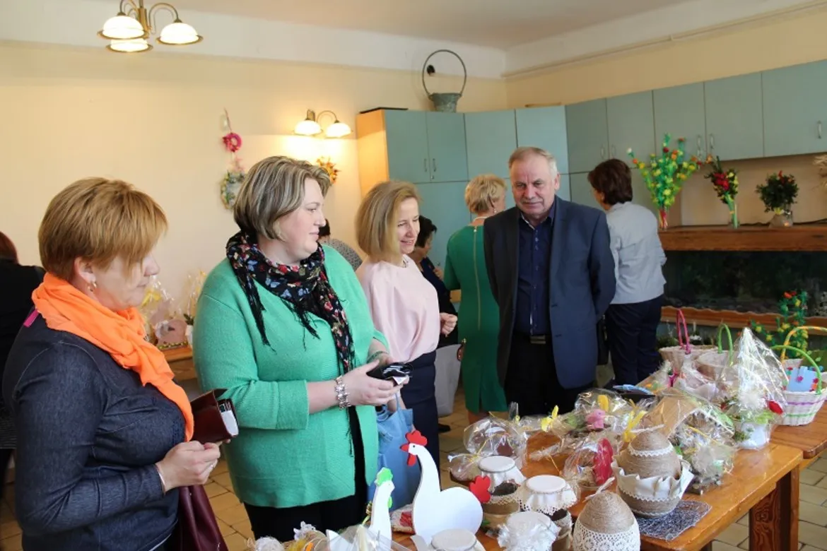 Uczestnicy spotkania wielkanocnego w DPS podziwiają dekoracje i rękodzieło na stole.