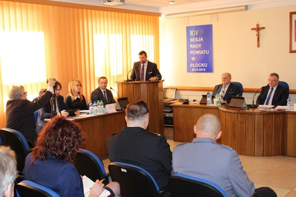 XIV sesja Rady Powiatu w Płocku, podczas której członkowie rady dyskutują przy stole konferencyjnym.