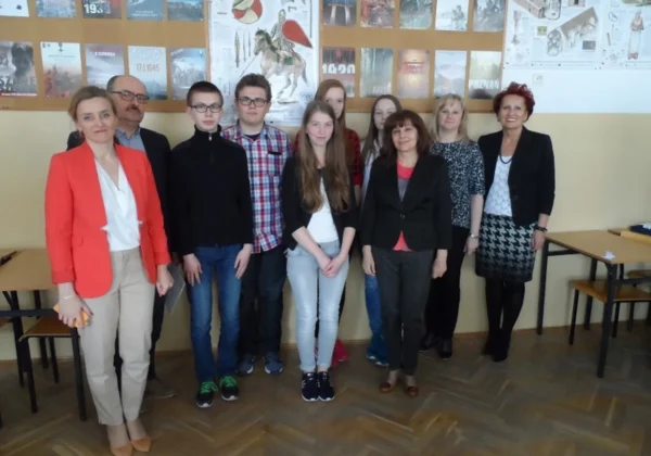 Grupa uczniów i nauczycieli podczas VIII Powiatowego Konkursu Historycznego stoi w szkolnej sali na tle tablicy z plakatami.