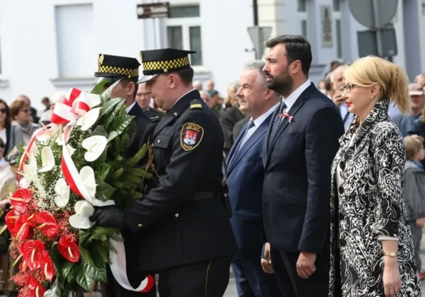 Uroczystość upamiętniająca 225. rocznicę uchwalenia Konstytucji 3 Maja – funkcjonariusze w mundurach składają wieniec kwiatów z biało‑czerwonymi wstążkami przed zgromadzonymi uczestnikami.