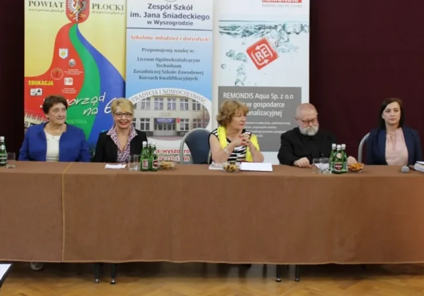 Pięć osób siedzi za długim stołem na scenie podczas III Nadwiślańskiego Dyktanda, w tle stoją plakaty i banery promujące wydarzenie.