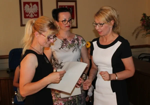 Trzy kobiety w sali konferencyjnej podczas wręczania certyfikatu jednej z nich na konferencji dla rodzin zastępczych z okazji Dnia Rodzicielstwa Zastępczego.