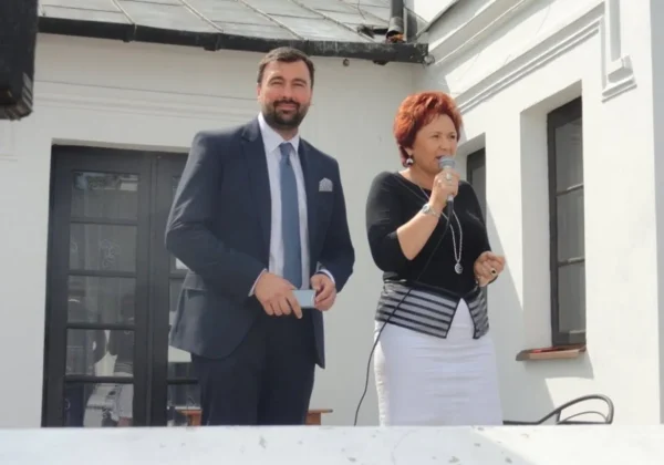 Para na scenie podczas obchodów 10-lecia Powiatowej Sekcji Emerytów ZNP w Płocku; mężczyzna w garniturze stoi obok kobiety z mikrofonem, która zabiera głos.