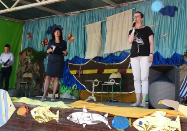 Na scenie podczas Letniego Pikniku Integracyjnego dwie kobiety mówią do mikrofonów, a w tle widoczna morska scenografia z łodzią i kolorowymi dekoracjami.