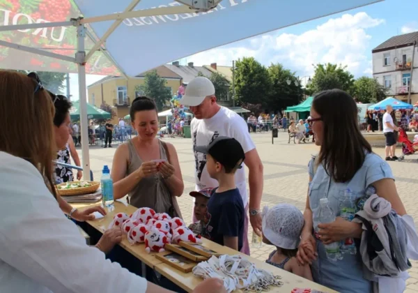 Grupa ludzi przy stoisku plenerowym podczas 37. Dni Wisły w Wyszogrodzie, w słoneczny dzień, rozdaje gadżety i rozmawia z rodzinami.