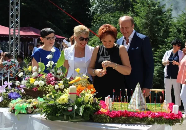 Grupa dorosłych osób stoi przy stole z kolorowymi kwiatami i dekoracjami podczas Nocy Świętojańskiej 2016 w Domu Pomocy Społecznej w Koszelewie.