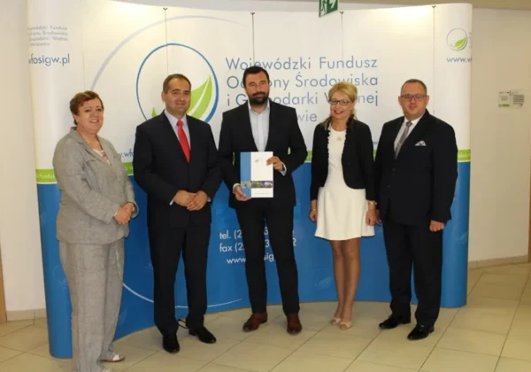 Pięć osób w formalnych ubraniach stoi przed banerem Wojewódzkiego Funduszu Ochrony Środowiska i Gospodarki Wodnej, prezentując projekt zagospodarowania terenów zielonych w powiecie płockim o wartości niemal 400 tys. zł.