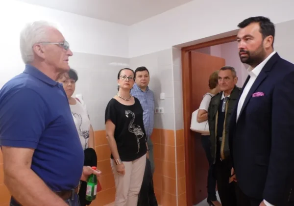 Grupa osób stoi w korytarzu nowej placówki opiekuńczo-wychowawczej w Wyszogrodzie, obserwując wnętrze przy białych i pomarańczowych ścianach i otwartych drzwiach.