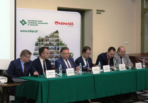 Grupa urzędników w garniturach siedzi przy zielonym stole podczas podpisywania umów dotyczących RIT i dofinansowania dróg w powiecie płockim, na tle banneru z mapą Mazowsza.