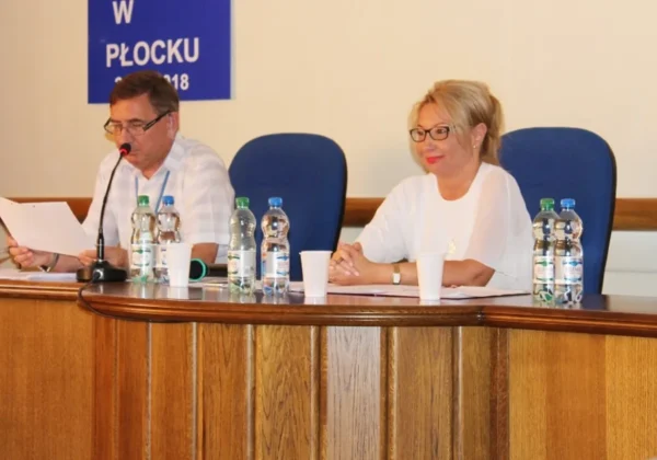 Dwóch urzędników siedzi przy drewnianym stole konferencyjnym z mikrofonem, dokumentami i butelkami wody podczas przygotowań powiatu do ćwiczeń obronnych Dolina Wisły – 2016.