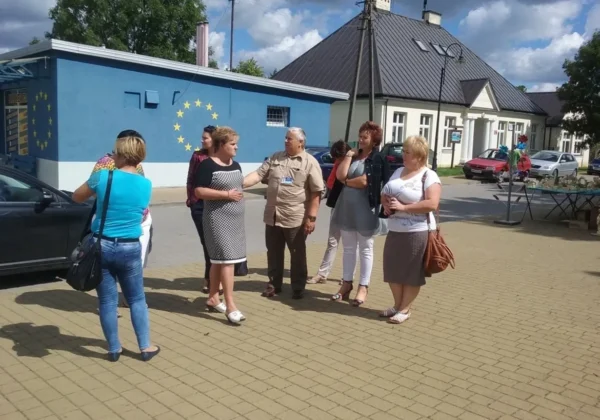 Grupa dorosłych stoi na placu festynu przed niebieskim budynkiem z motywem Unii Europejskiej, rozmawiając.