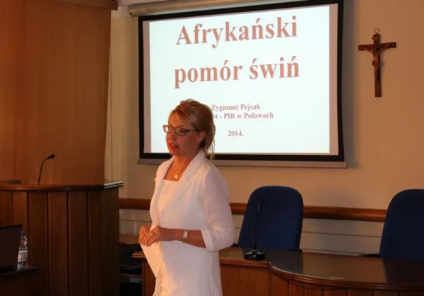 Kobieta w białej marynarce prowadzi prezentację w sali konferencyjnej, a na projektorze wyświetla się slajt o Afrykańskim pomorze świń.
