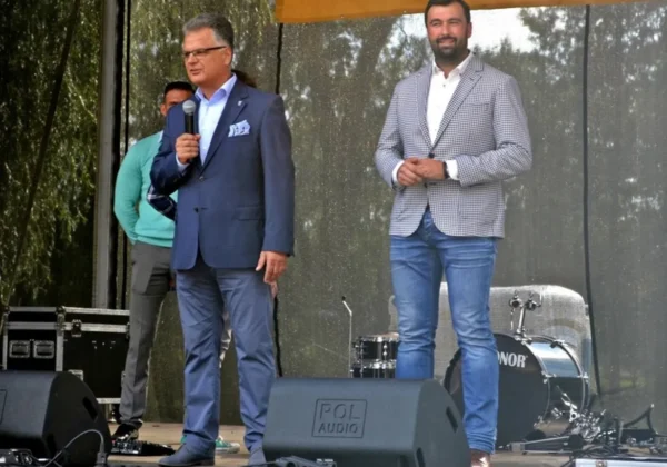 Dwóch mężczyzn na scenie podczas Dni Bodzanowa; jeden przemawia do mikrofonu, drugi stoi obok z uśmiechem, w tle sprzęt muzyczny i perkusja.