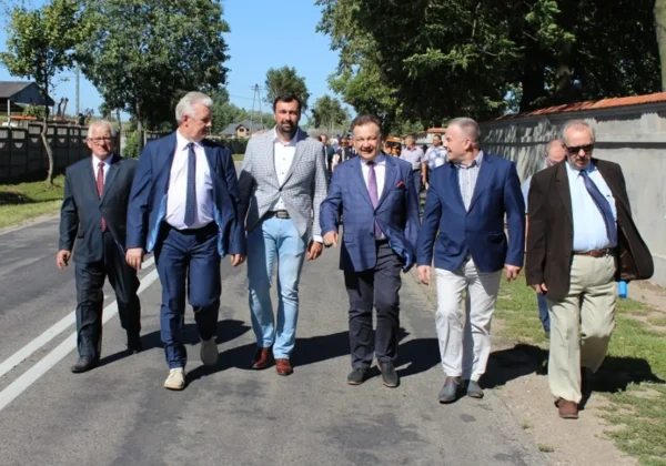 Grupa urzędników w garniturach spaceruje po drodze podczas inspekcji remontu Drogi Wojewódzkiej nr 575.