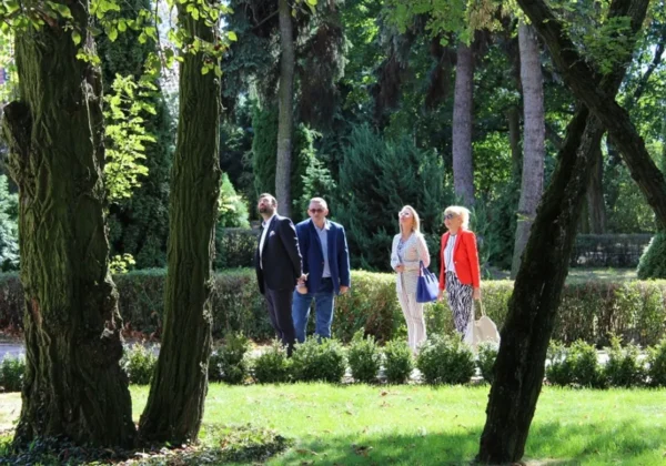 Grupa czterech osób w eleganckich strojach spaceruje po parku wśród drzew i krzewów, w kontekście realizacji unijnych projektów w powiecie płockim.
