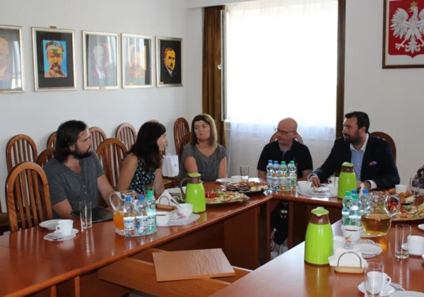 Grupa studentów z Węgier siedzi przy stole w sali konferencyjnej Starostwa Powiatowego w Płocku podczas wizyty, rozmawiają przy kawie i przekąskach.