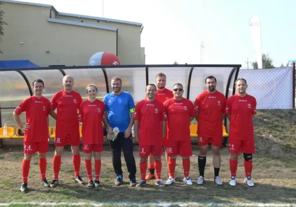 Grupa piłkarzy w czerwonych strojach stoi przed ławką rezerwowych na nowo otwartym stadionie w Bulkowie.