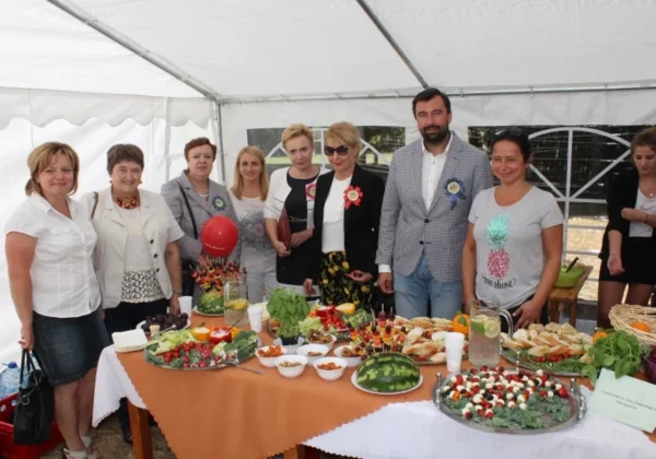 Grupa osób stojących za stołem pełnym różnorodnych potraw i napojów podczas Powiatowego Dnia Promocji Zdrowia w Brwilnie, pod białym namiotem.