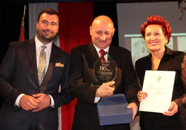 Scena z uroczystości 110. rocznicy Jagiellonki: trójka osób w garniturach, w tym mężczyzna pośrodku trzyma przezroczysty, diamentowy puchar z napisem 110 lat, a kobieta po prawej trzyma teczkę z napisem Starosta Płocki.