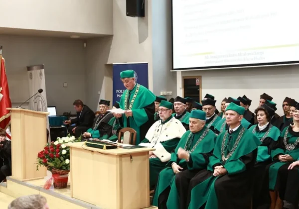 Uroczystość 50. inauguracji Politechniki Warszawskiej Filii w Płocku: profesorowie i doktorzy w zielonych togach siedzą na scenie podczas przemówienia z mównicy.