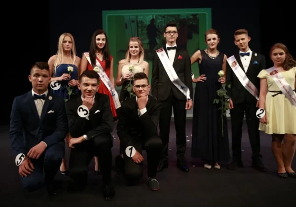 Grupa młodych finalistów Miss i Mister Wolontariatu 2016 stojących na scenie płockiego Teatru podczas gali, ubranych w wieczorowe stroje, trzymających kwiaty i noszących numerki.