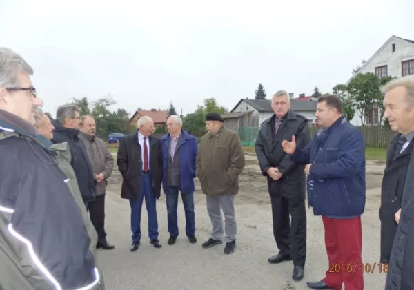 Grupa strażaków ochotników z całej Polski wraz z lokalnymi gośćmi stoi na placu podczas wizyty w Powiecie Płockim.