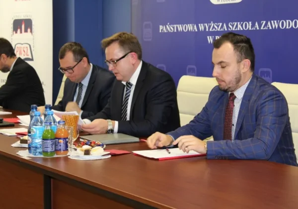 Czterech mężczyzn w garniturach siedzi przy długim stole w sali konferencyjnej podczas pierwszego posiedzenia Konwentu Państwowej Wyższej Szkoły Zawodowej w Płocku w kadencji 2016–2020, przeglądając dokumenty.