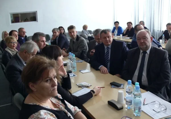 Grupa osób w formalnych ubraniach siedzi przy długim stole w sali konferencyjnej, omawiając reformę edukacji podczas spotkania w Płońsku.