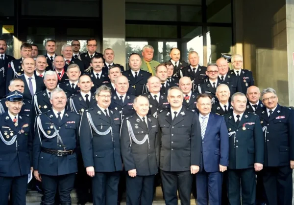 Grupa strażaków w mundurach z odznaczeniami stoi na schodach przed wejściem do budynku podczas IV Zjazdu Oddziału Powiatowego strażaków.